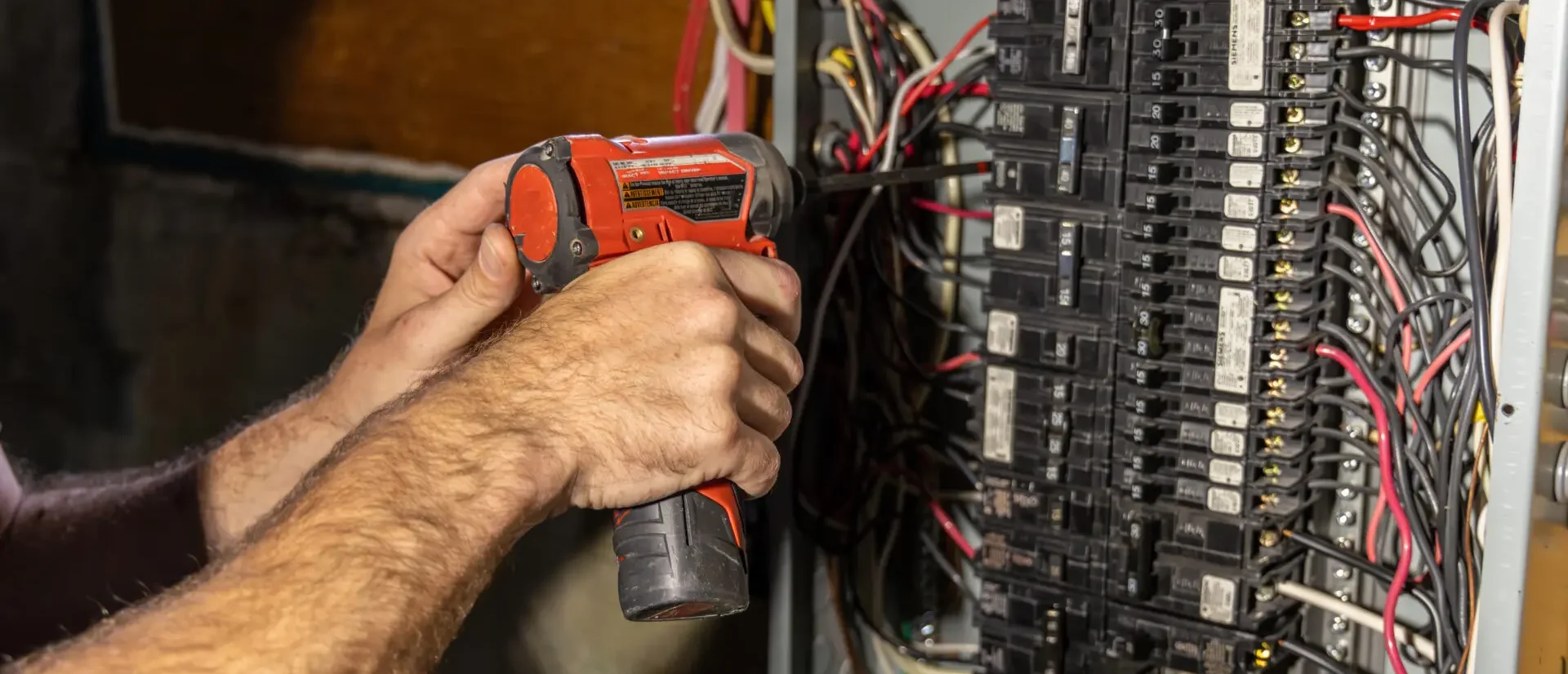 Electrician using a power drill to work on wiring inside a residential electrical breaker panel.
