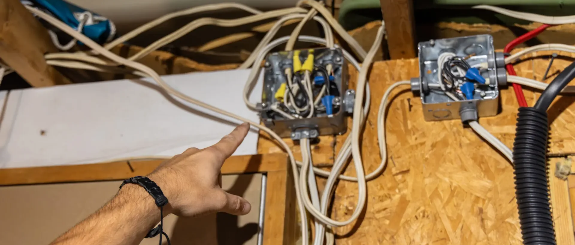 Person pointing at electrical junction boxes with exposed wiring in a wooden wall.