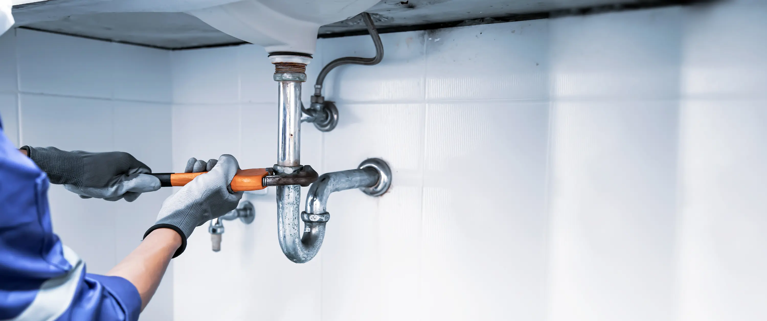 Plumber using a wrench to repair a water pipe under the sink