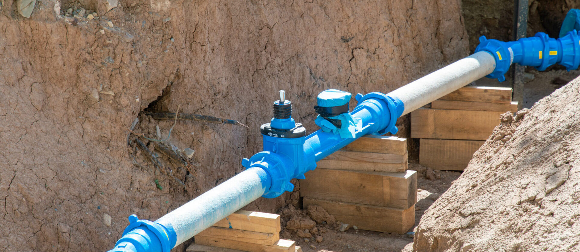 Underground water pipeline with blue valve fittings supported by wooden blocks during installation.
