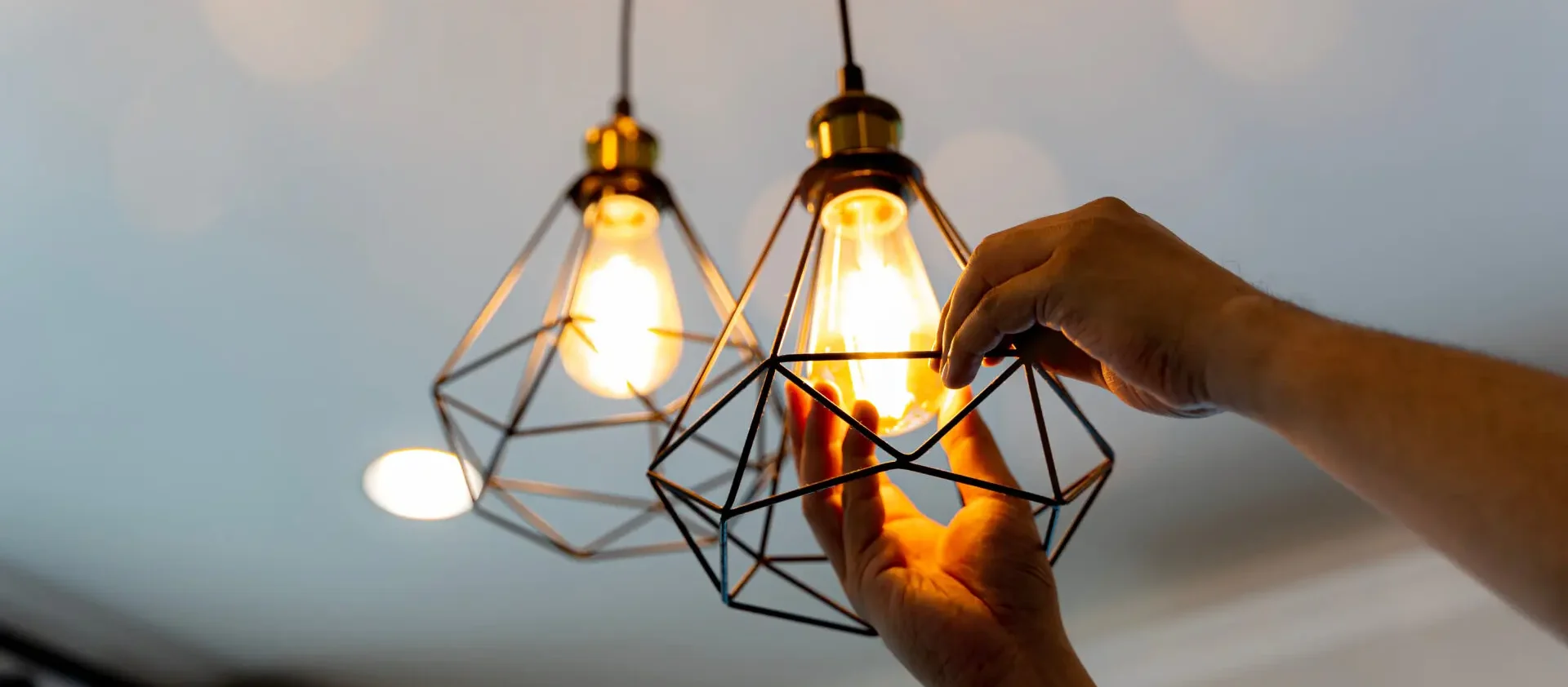 Person installing or adjusting a light bulb inside a modern geometric pendant light fixture.