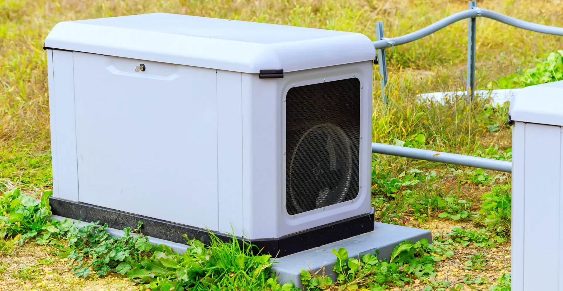 Outdoor standby generator installed on a concrete pad in a grassy area.