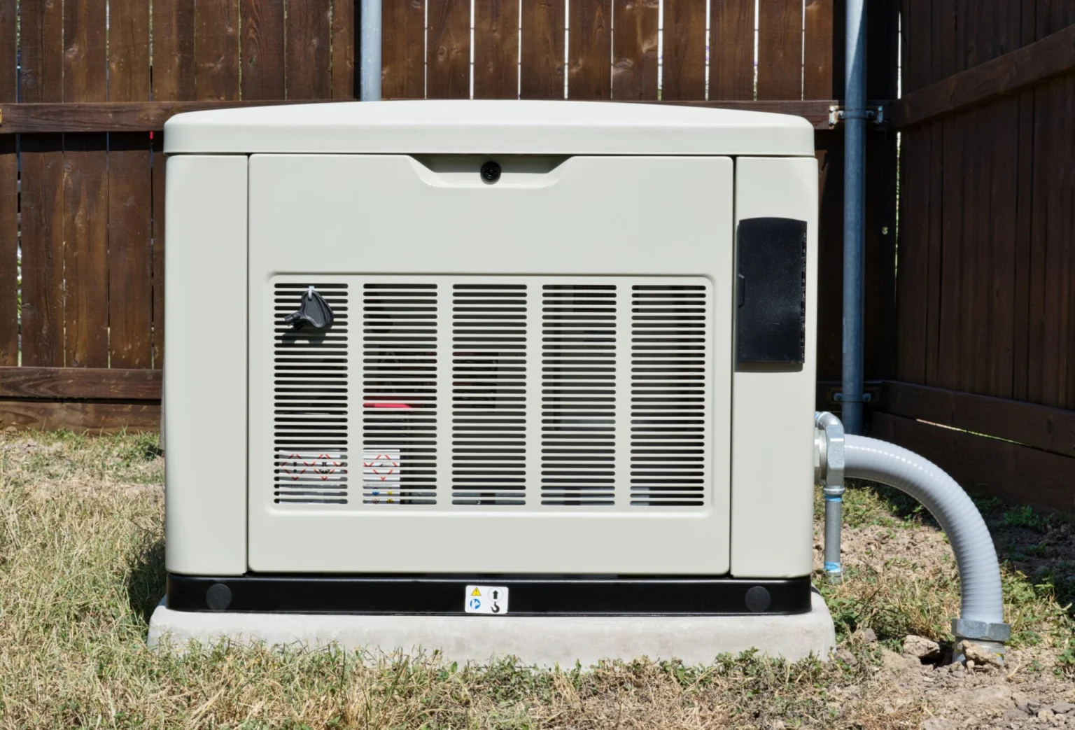 Standby generator installed on a concrete pad next to a wooden fence.